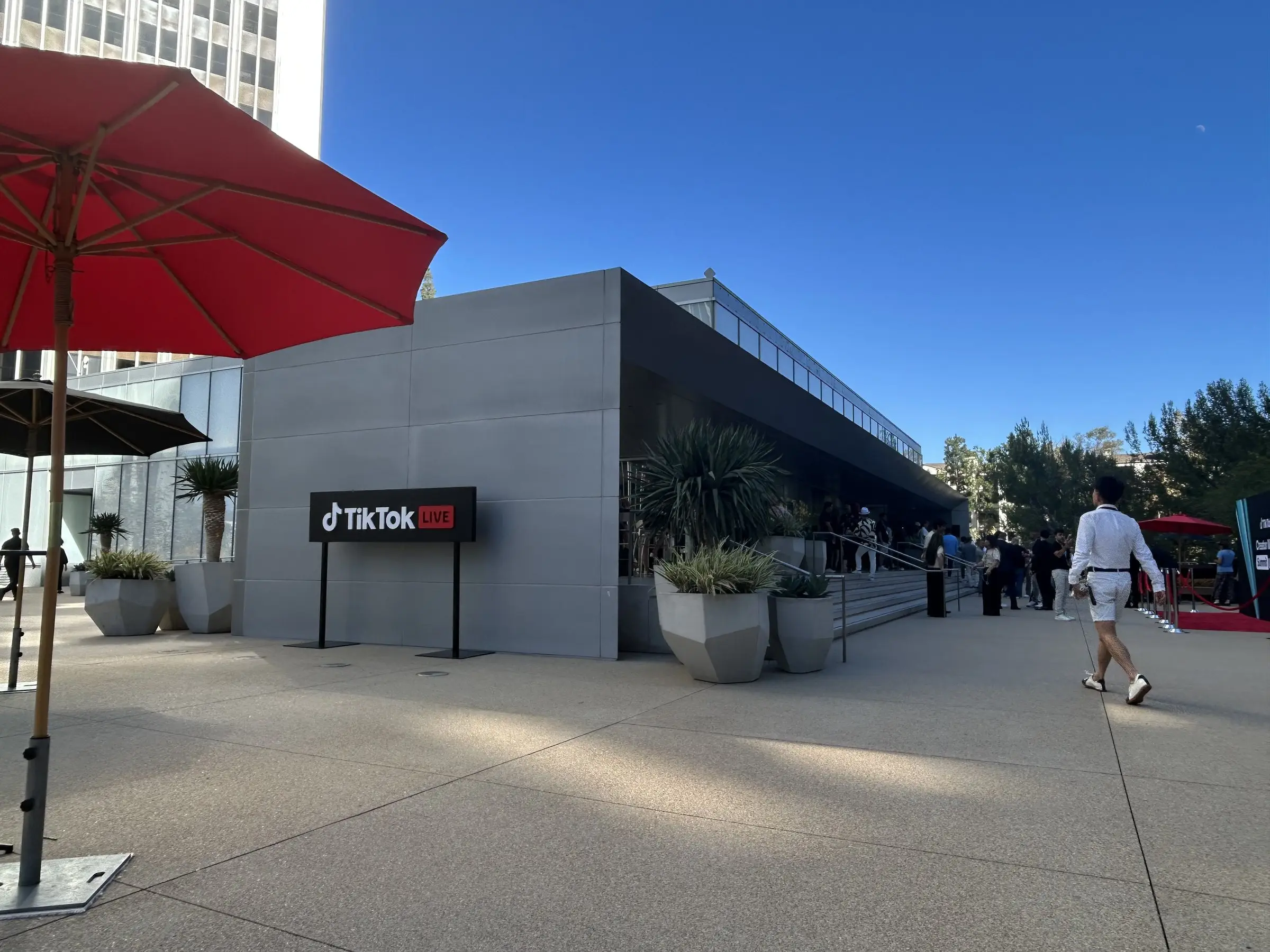 The outside of the pavilion in daylight, a low gray building with the TikTok Live sign on the corner and patio umbrellas nearby.