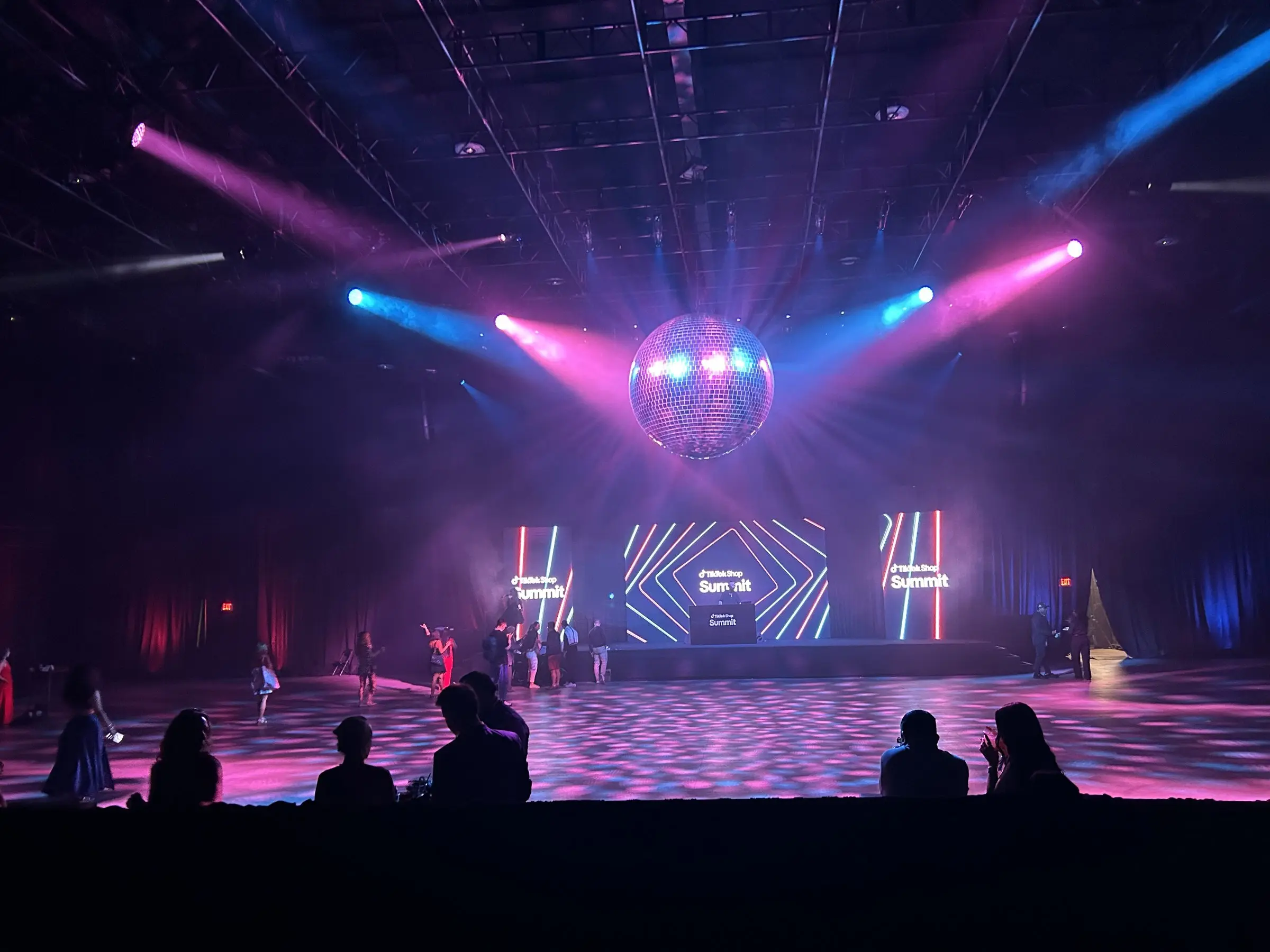 Beams cut through haze from the overhead rig, catching the mirror ball above the LED wall while guests watch from the floor.