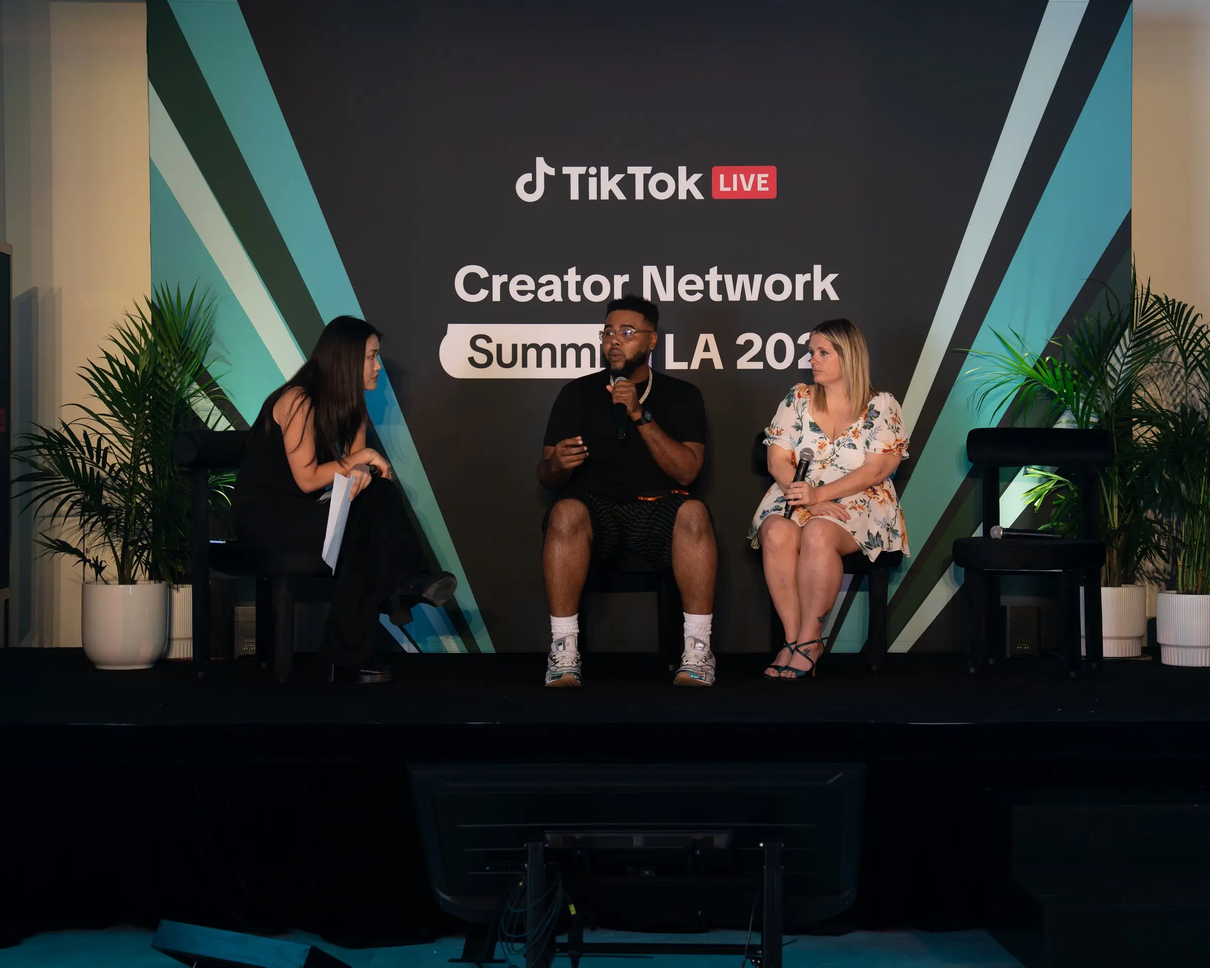 Three panelists with microphones on the low stage in front of the branded LED wall reading Creator Network Summit LA 2026, potted palms on both sides.
