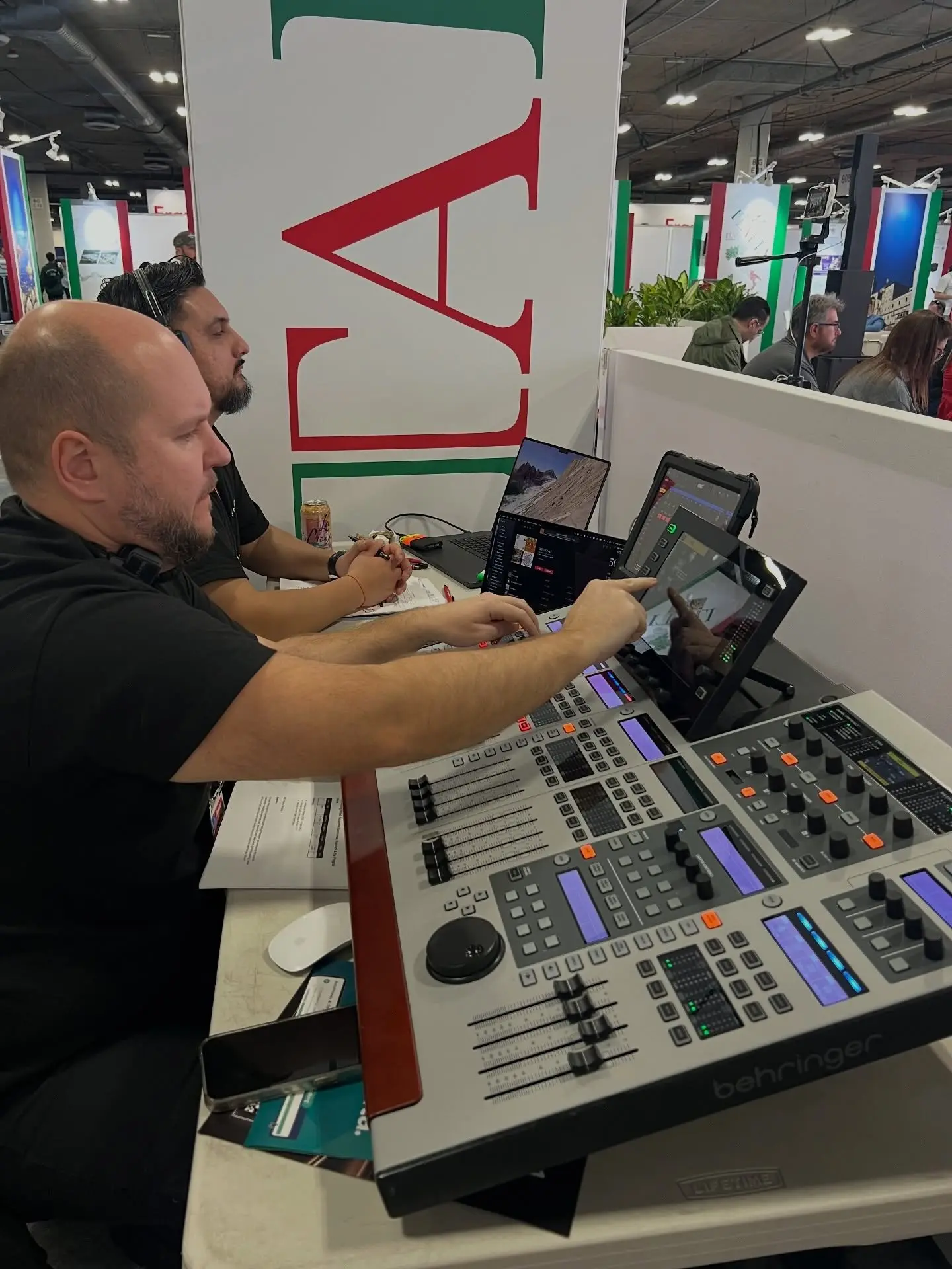 A crew member at an audio console on the stand, tablets and a laptop set up beside the faders.