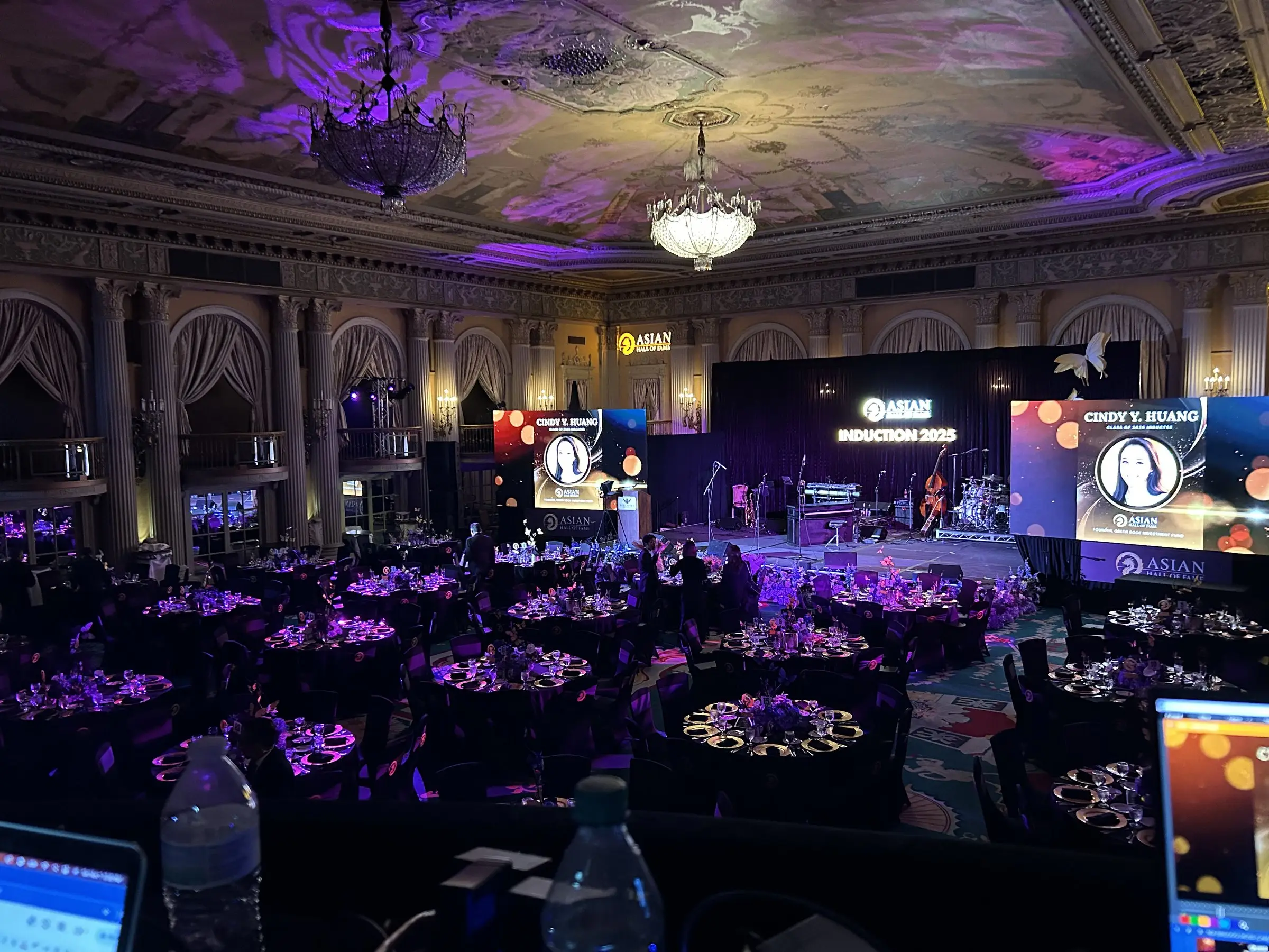 Two side LED screens flank the main stage while uplights throw magenta across the ceiling and the tables below.
