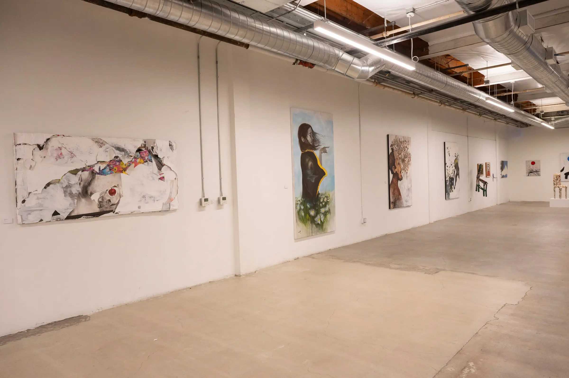 Paintings hung down a long white wall under the exposed ducts and strip lights of the gallery.
