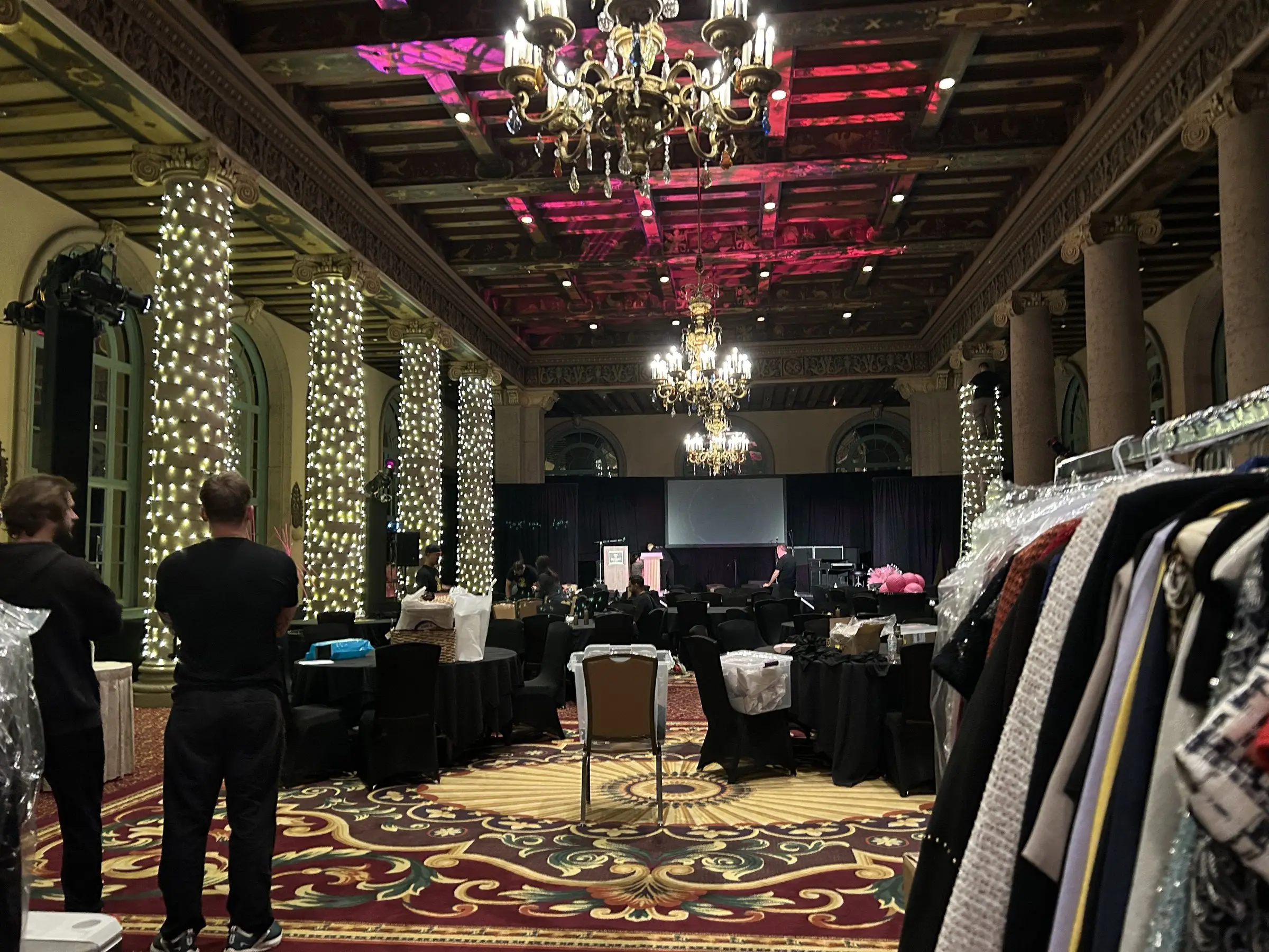 A corner of the room being set, clothing racks along the wall, lit columns behind, and a patterned carpet running the length of the floor.