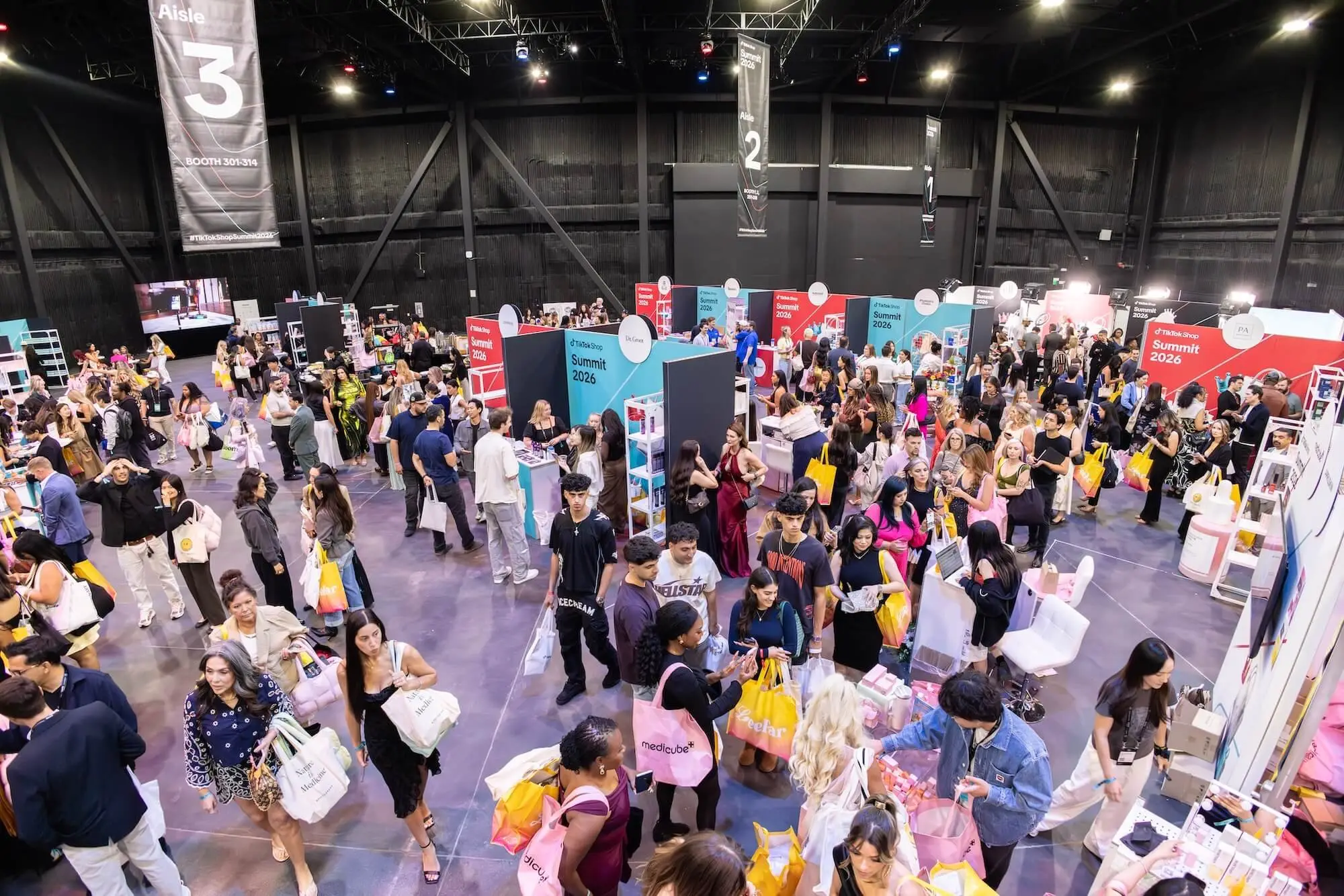 A view down onto the expo floor, exhibitor booths lining the aisles and a dense crowd moving between them.