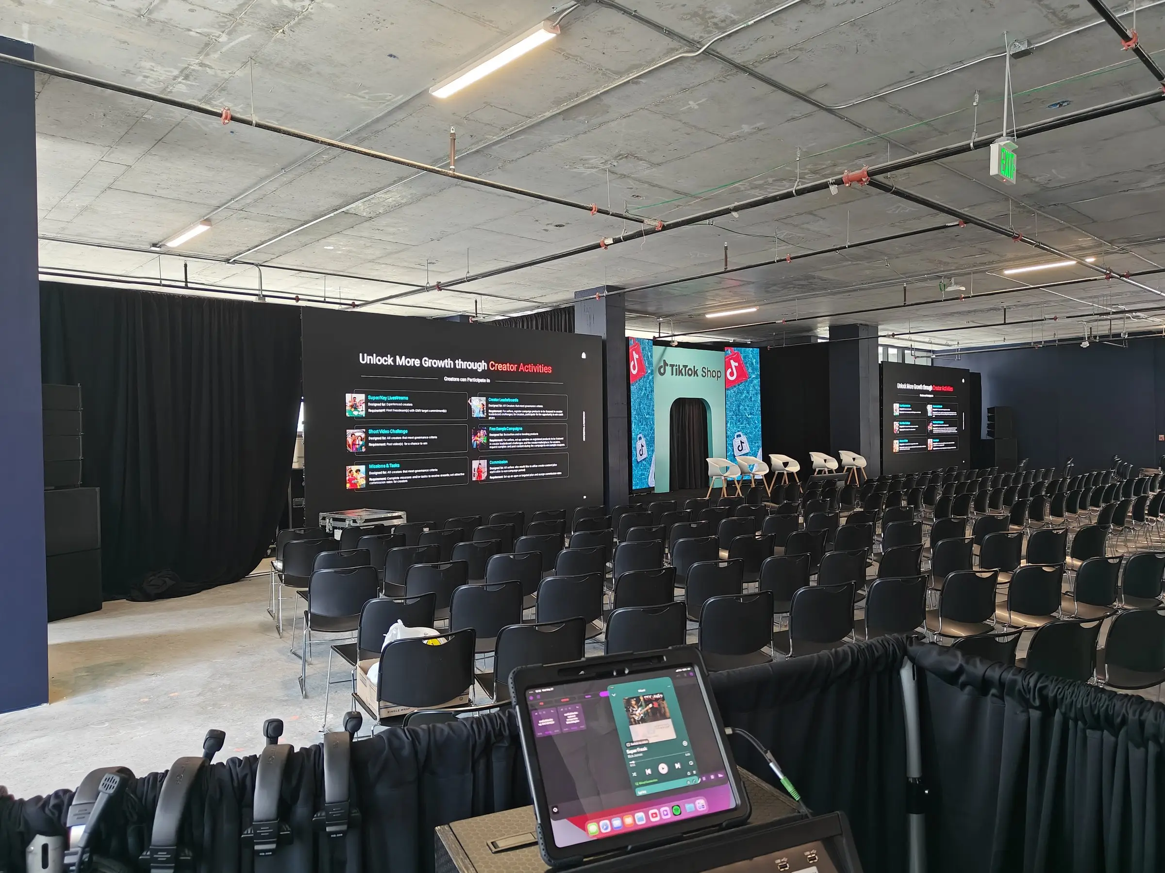 The session room seen from the tech position at the back, rows of black chairs facing a TikTok Shop LED backdrop between two printed content walls.