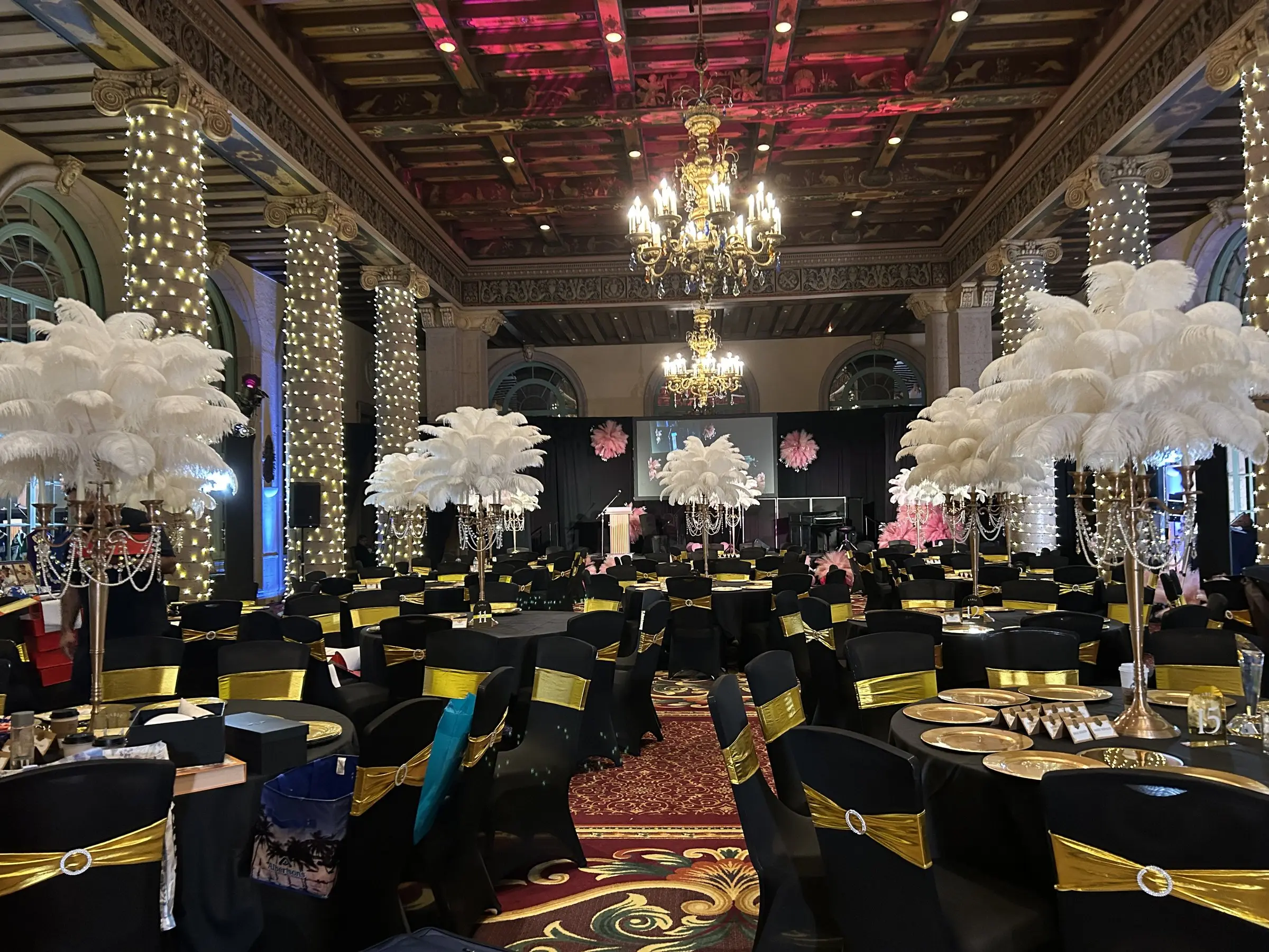 Tables dressed in black with gold chair sashes and tall feather centerpieces, the ceiling washed red above.
