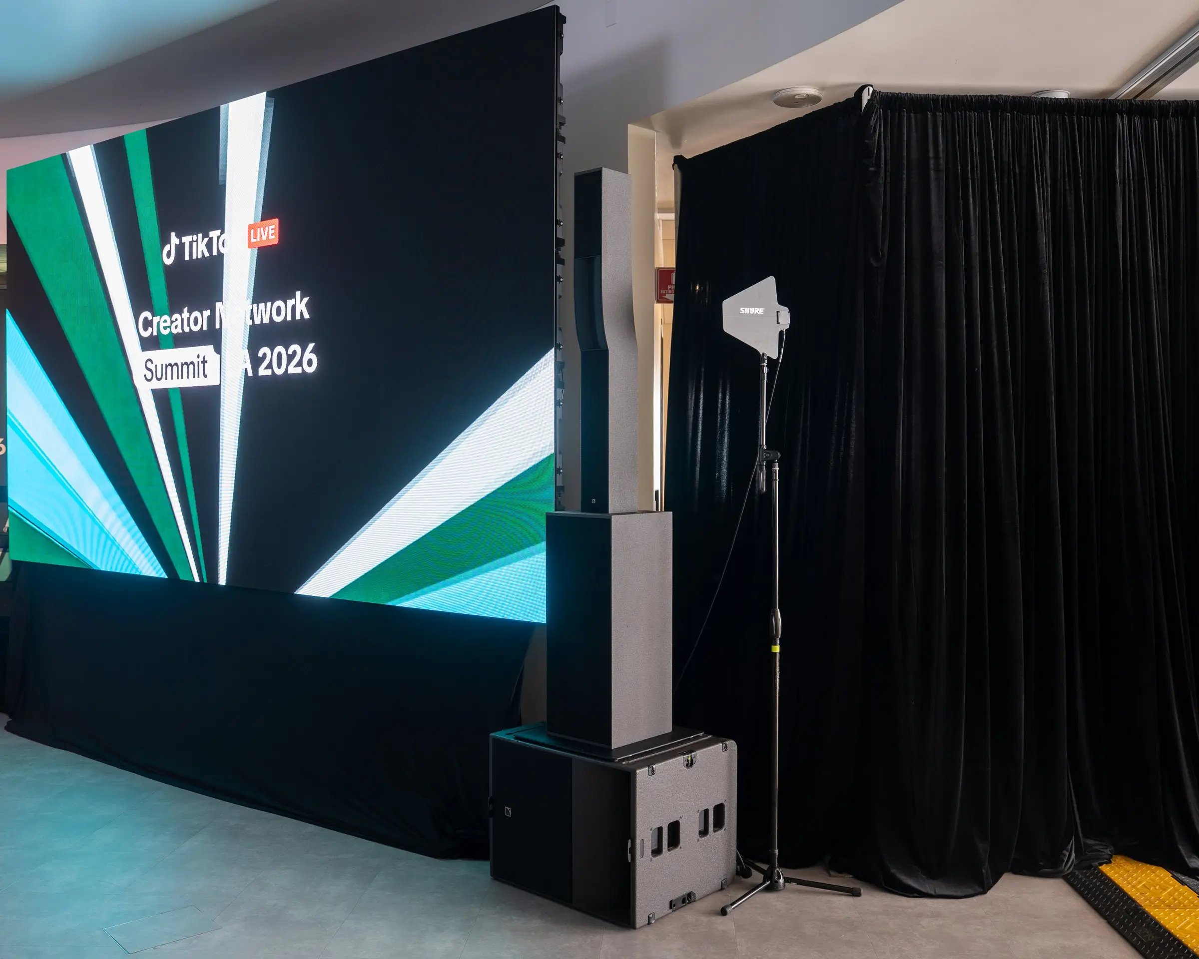 One LED wall running the summit graphic beside a line array and a subwoofer, with a wireless antenna on a stand against black drape.