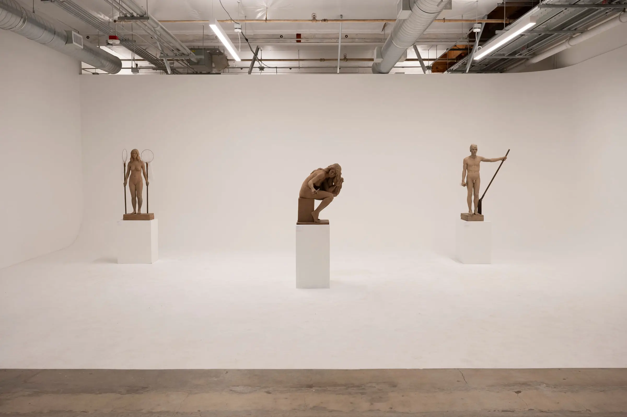 Three carved figures on plinths in the corner of a white cyclorama room.