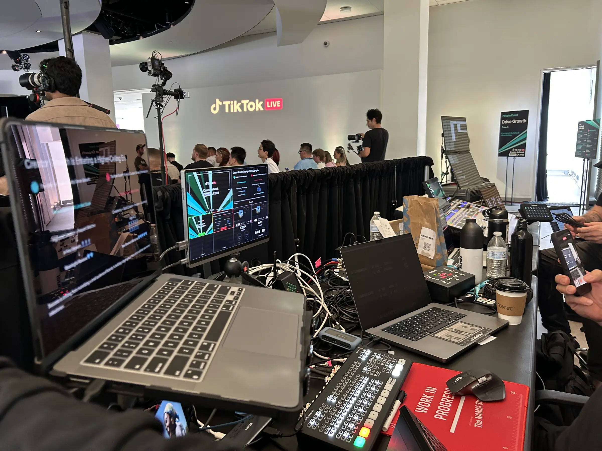 The tech position at the back, laptops, a video switcher, and preview monitors on a draped table beside the TikTok Live sign.