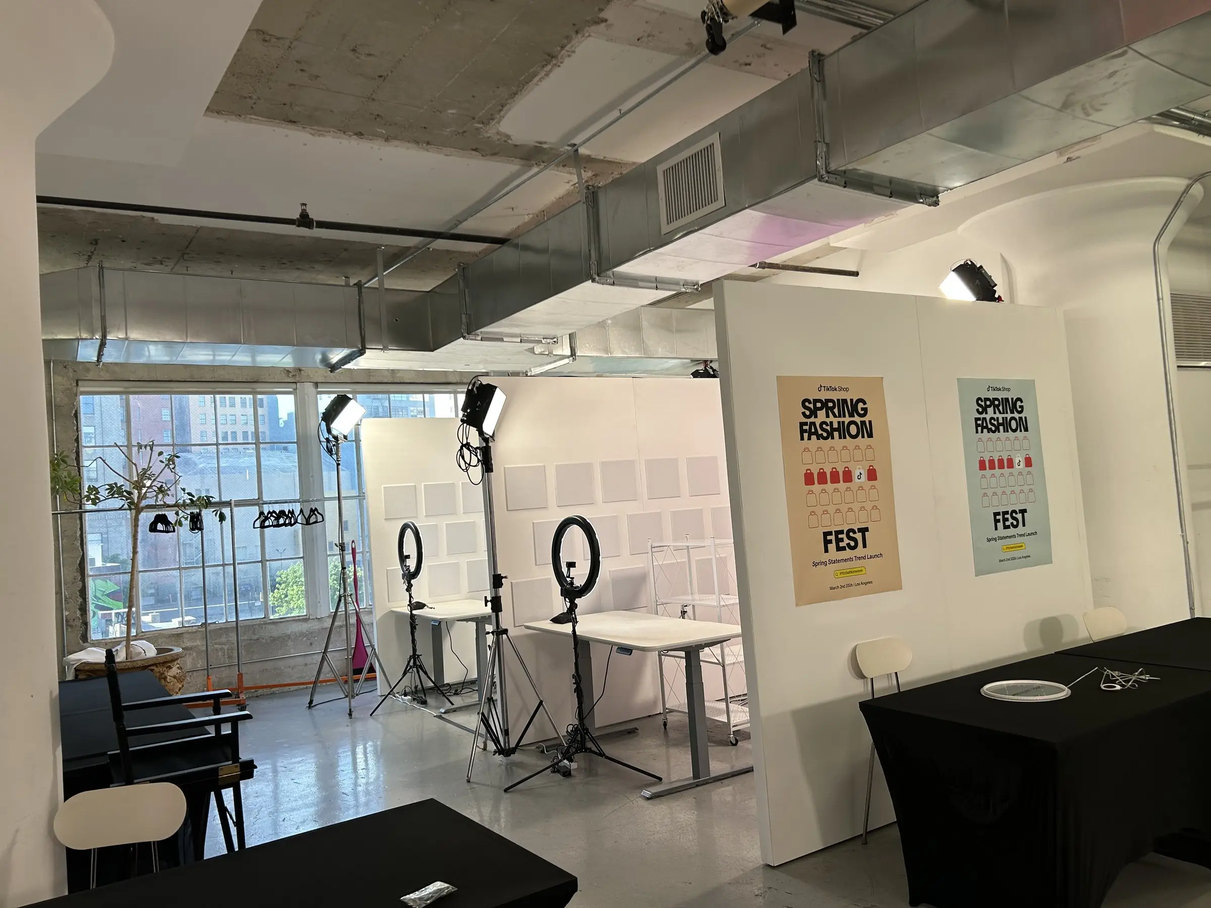 An empty room set for filming, ring lights and stands on the floor, printed posters on the wall, daylight coming through the windows.