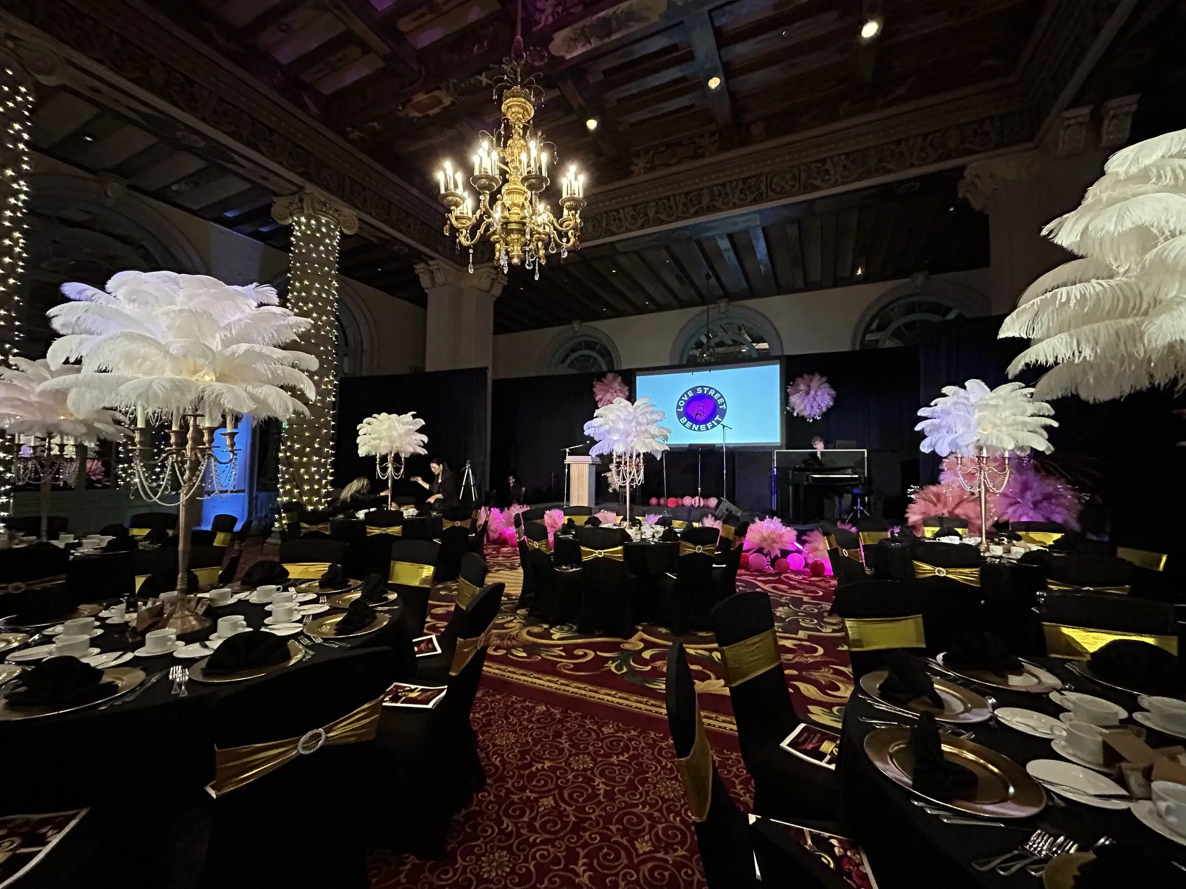 A view down the room toward the stage, feather centerpieces framing both sides and the screen lit at the end.