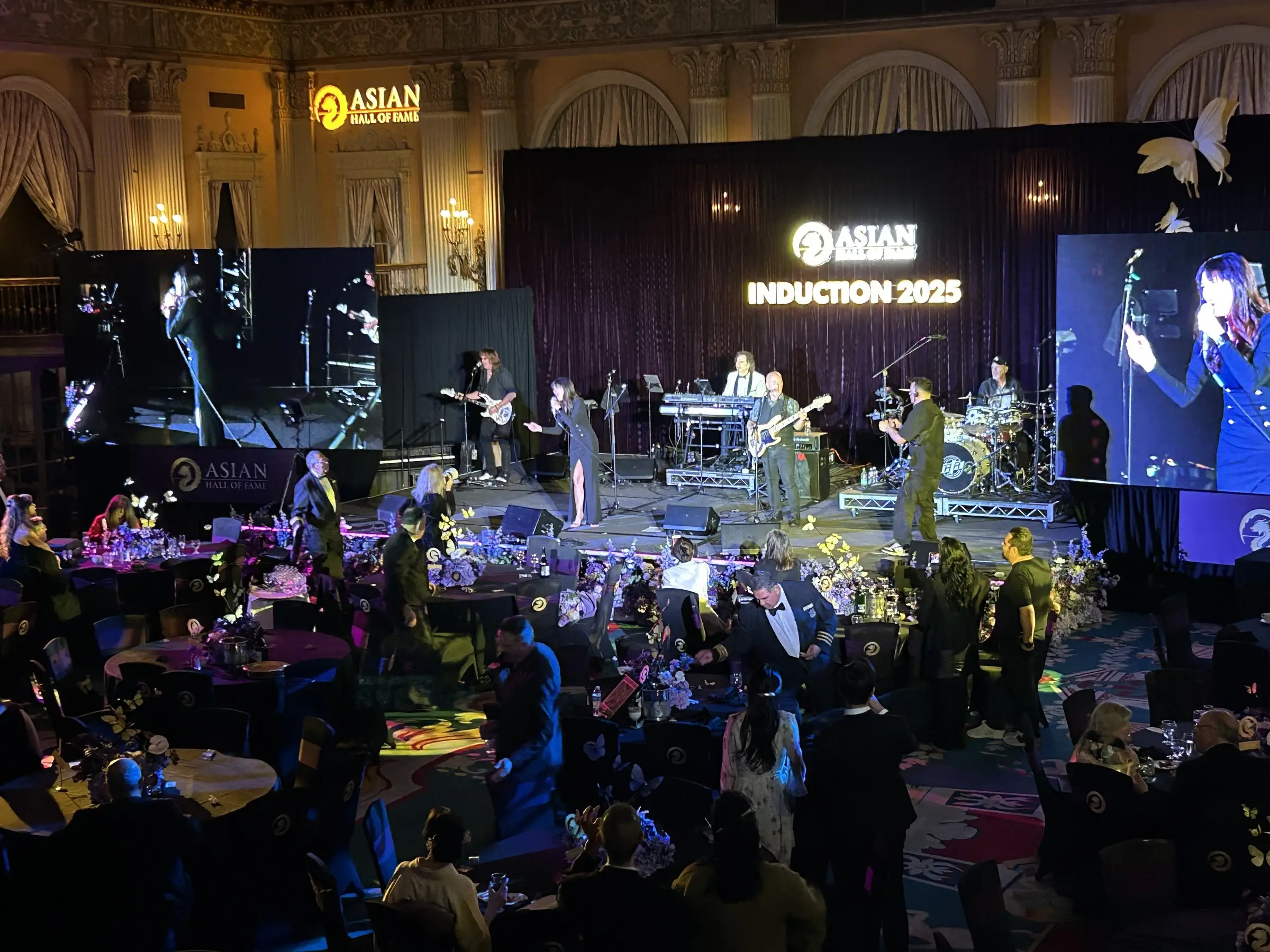 The stage from the floor, a full band in front of an LED wall reading Induction 2025, with guests seated in the foreground.