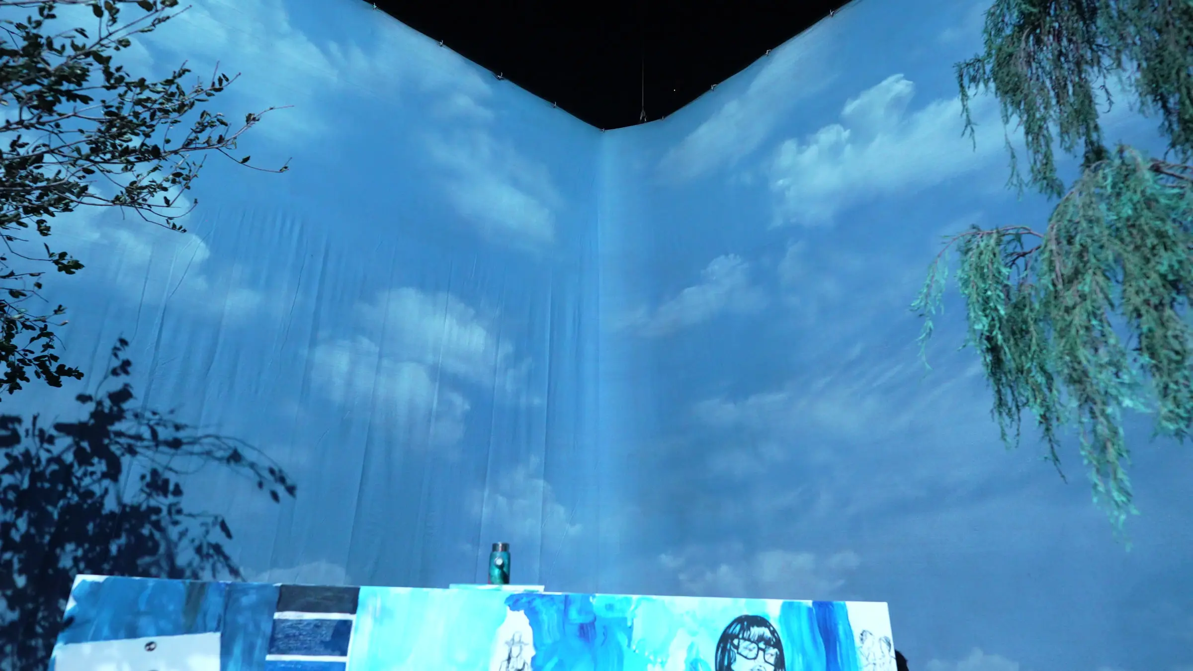 The corner of the draped perimeter with a sky and cloud image projected across both walls, willow branches hanging into the top of the frame.