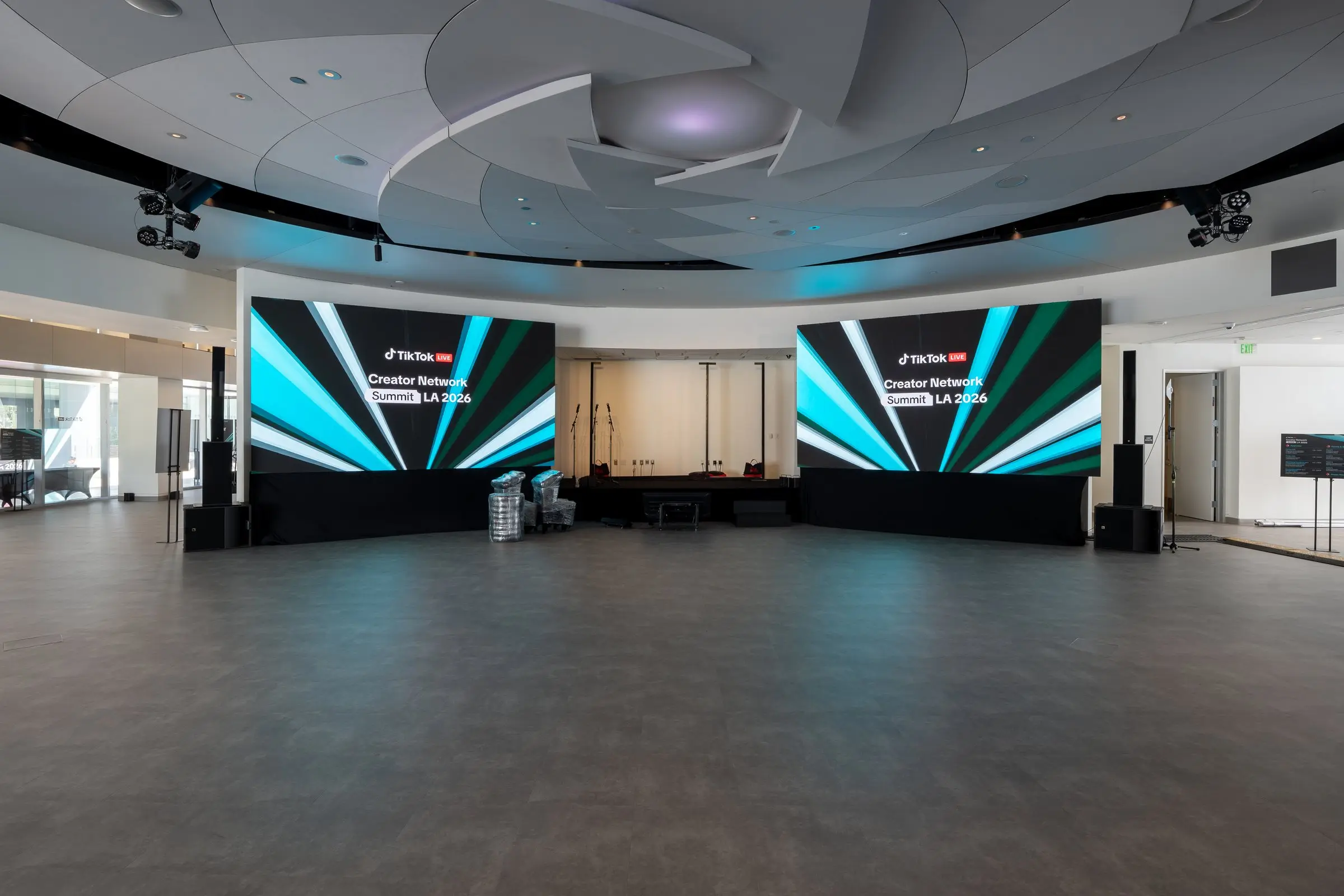 The room during build with the floor still bare, both LED walls lit with the summit graphic under the sculpted ceiling.
