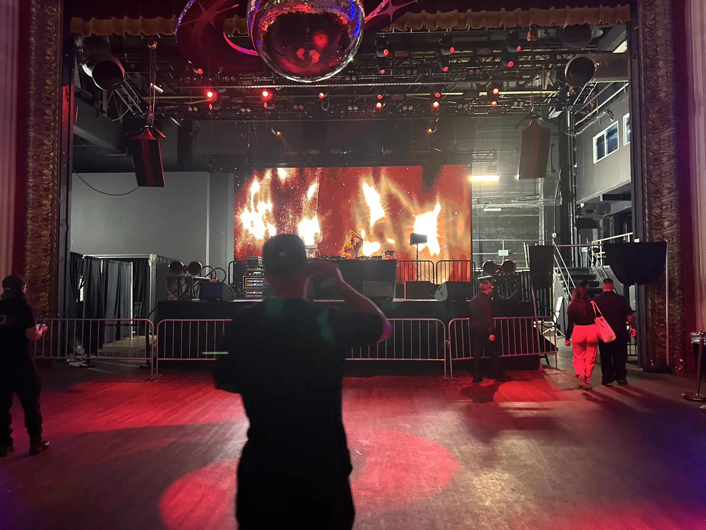 The show running, a wall of fire graphics on the LED screen and a crowd along the barricade under red light.