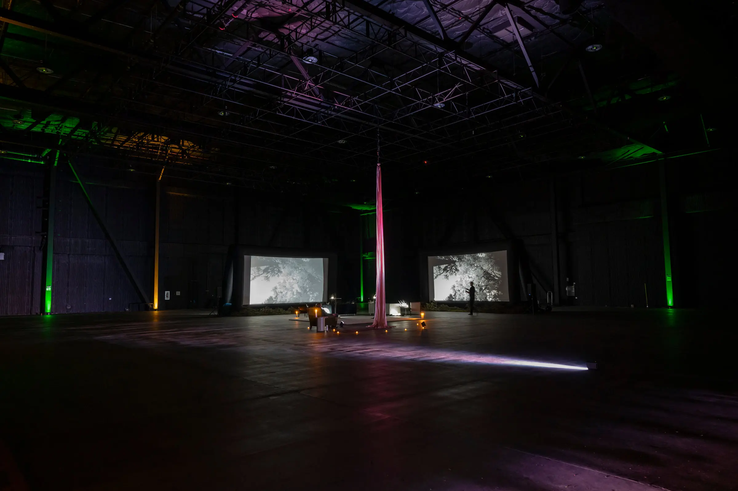 A dark hall under the truss grid, a length of pink silk hung from the rig between two projection screens, with candles on the floor and green uplights on the walls.