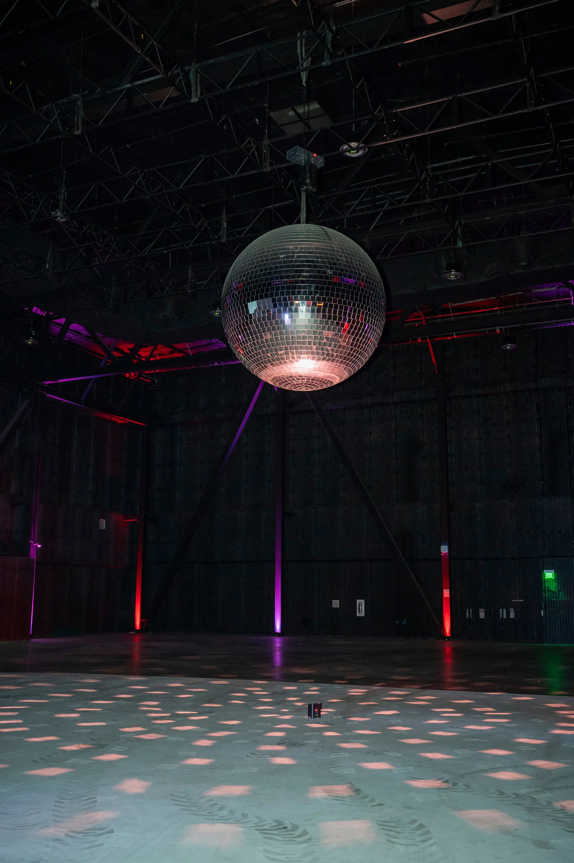 The mirror ball on its motor under the steel grid, red and magenta uplights along the wall and the light spread across the floor below.