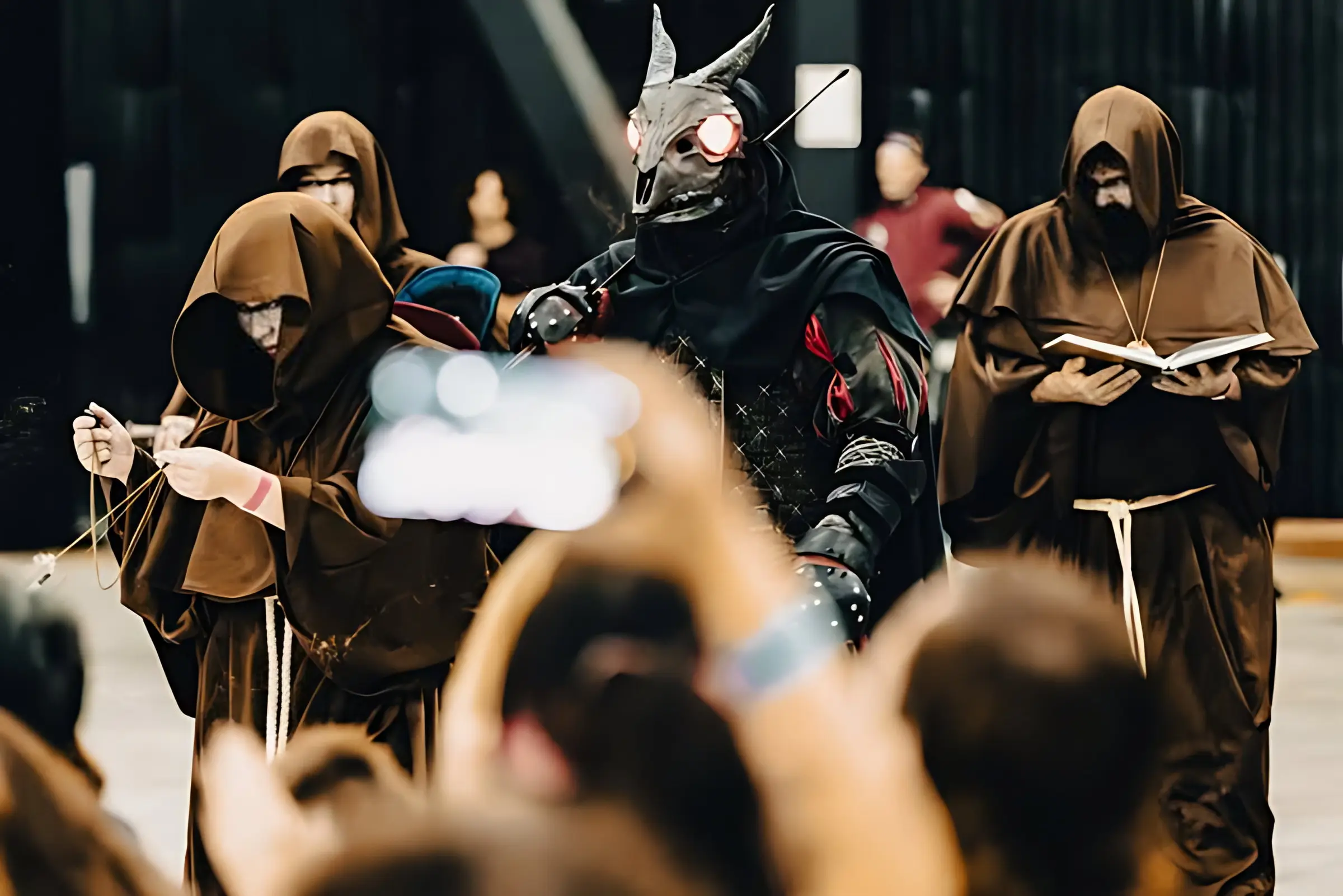 Robed figures in hoods carrying censers and a book into the ring, one of them in a horned mask, with the audience watching in the foreground.