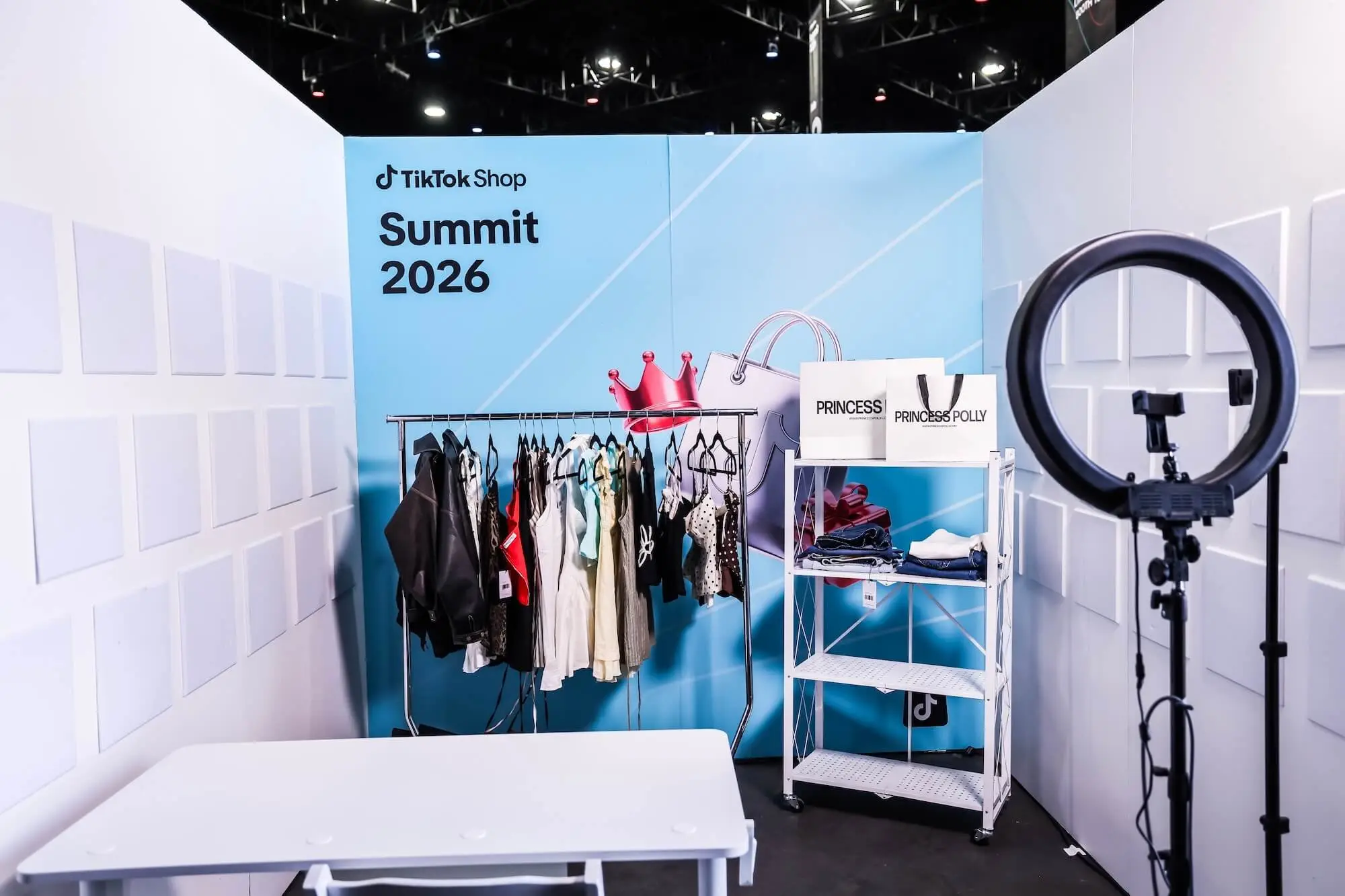 A live selling booth with a clothing rack, a ring light on a stand, and a blue printed backdrop reading Summit 2026.
