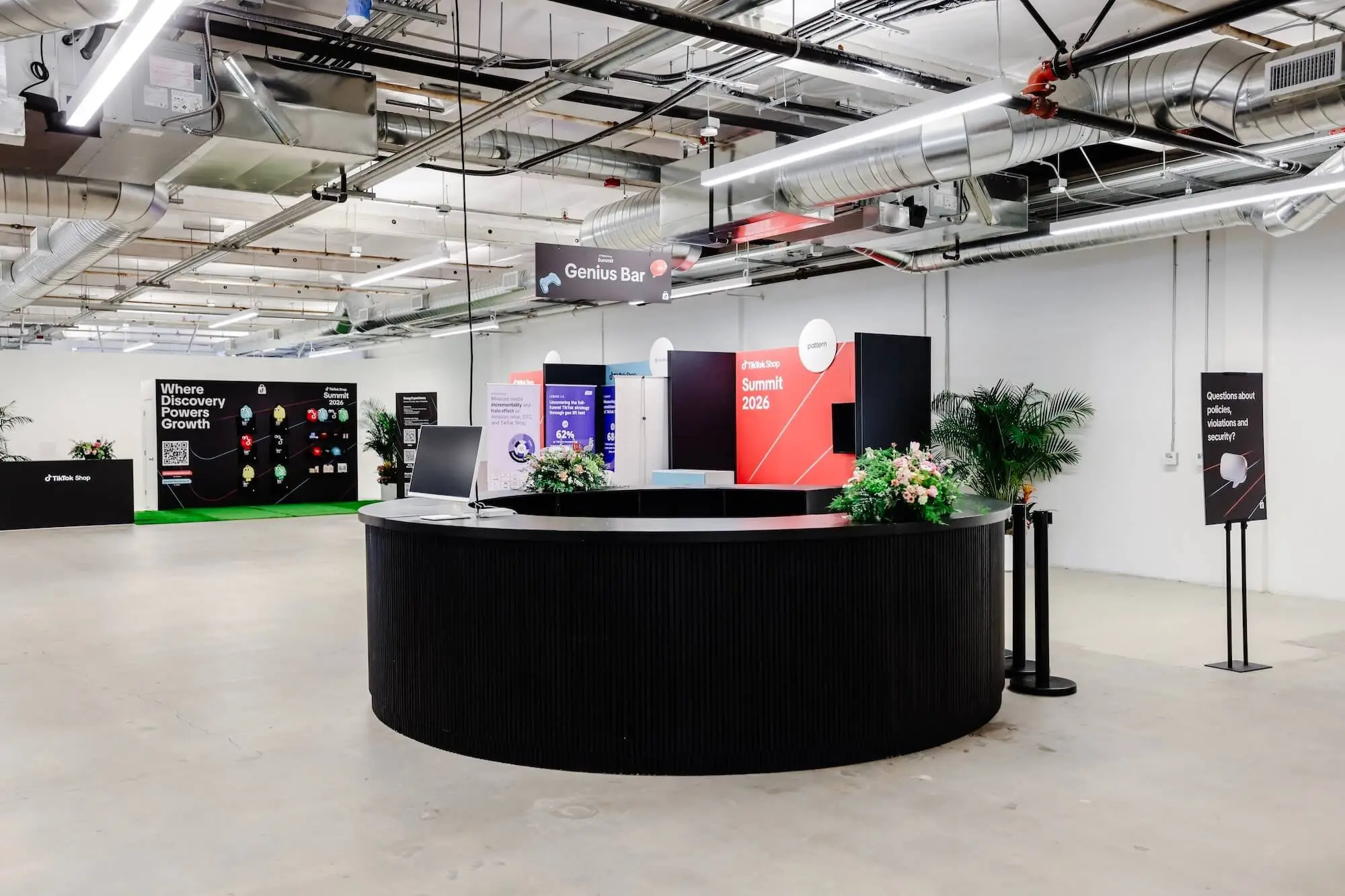 A round black welcome desk in a white room, plants at either side and content screens on the wall behind it.