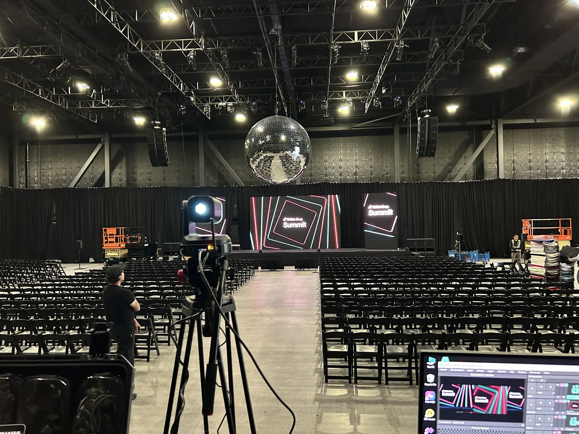 The broadcast position during load-in, a camera on a tripod and control monitors facing the stage across rows of empty chairs under the mirror ball.