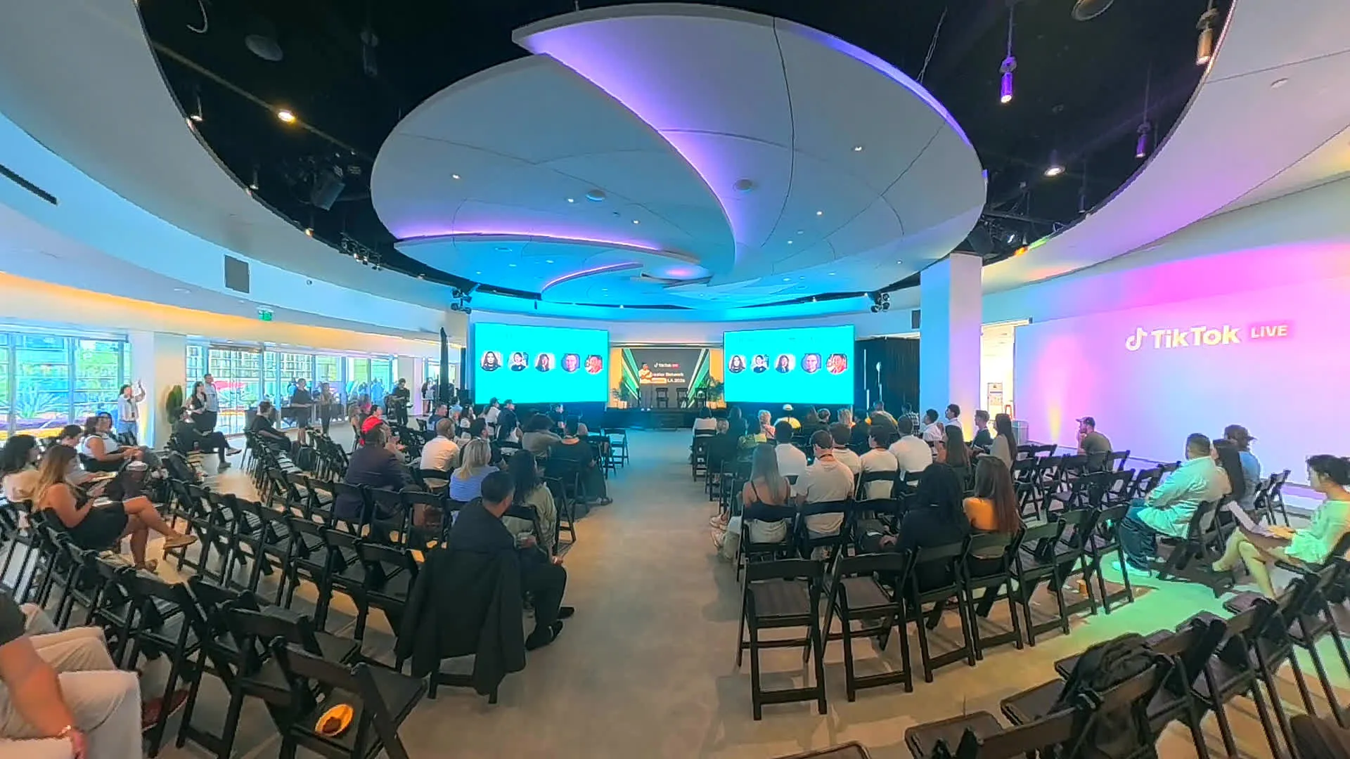 The summit floor from the back corner, the sculpted ceiling washed purple over a full audience, two screens running the panel and the TikTok Live logo glowing on the far wall.