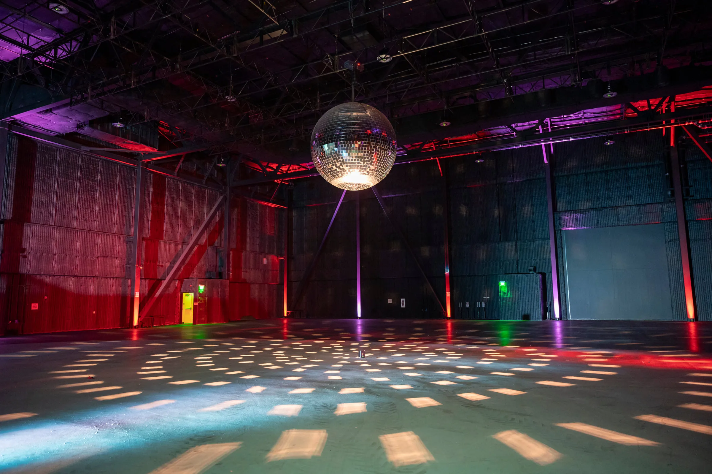 A mirror ball hung from the grid over an empty soundstage floor, its light spread across the concrete, with red, magenta and green uplights along the walls.